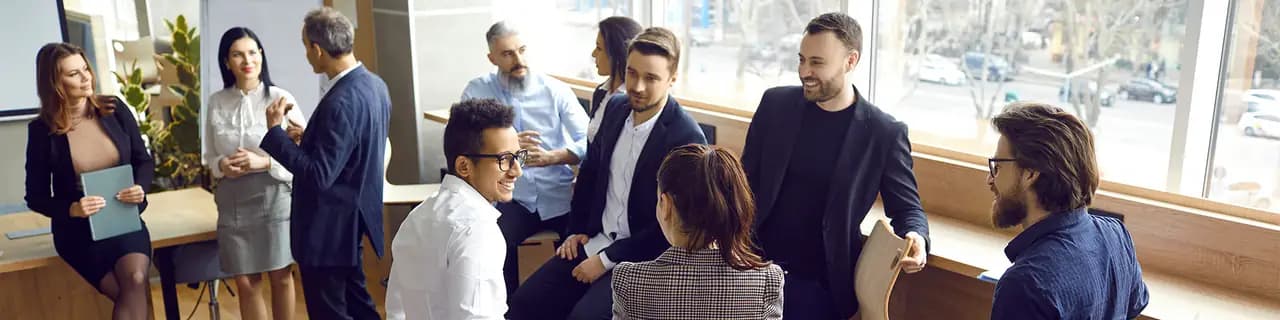 Plusieurs personnes échangent debout dans un bureau lumineux ; certaines sont assises, d'autres appuyées contre une table.